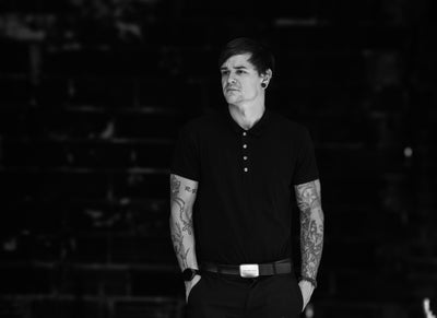 Robb Ramsden founder of The Rebuild Code wearing a black polo shirt with tattoos on arms against a dark background. The founder of the first ever Identity Rebuild Systems.